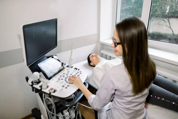 Visão do ângulo lateral da jovem médica no casaco branco que realiza o exame de ultra-som do abdômen para uma paciente do sexo feminino . — Fotografia de Stock
