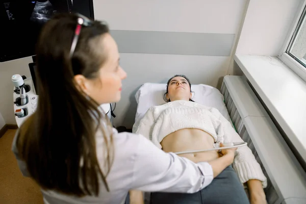 Профессиональный врач осматривает женский живот и почки с помощью ультразвукового оборудования. Молодая кавказка проходит обследование на ультразвуке — стоковое фото