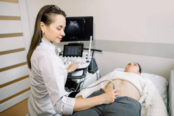 Médica muito feminina operando scanner de ultra-som moderno enquanto examina a barriga e a bexiga de sua paciente feminina — Fotografia de Stock