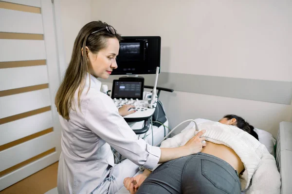 УЗИ в физиотерапии. Молодая женщина-терапевт использует ультразвуковой сканер на нижней части спины пациентки. УЗИ спины и почек — стоковое фото