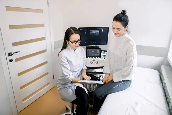 A jovem médica sorrindo conversando com paciente do sexo feminino em seu consultório, na sala de exame de ultra-som. Médico e paciente após o teste de ultra-som, falando — Fotografia de Stock