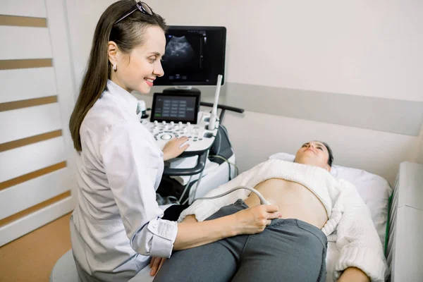 Female doctor performs ultrasound examination of pelvic organs of her female patient for diagnostic early pregnancy at the medical office Stock Photo