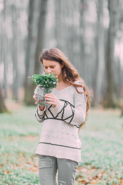 Bela jovem mulher caminhando pela floresta verde na primavera, segurando ar de vidro com flores brancas da primavera — Fotografia de Stock