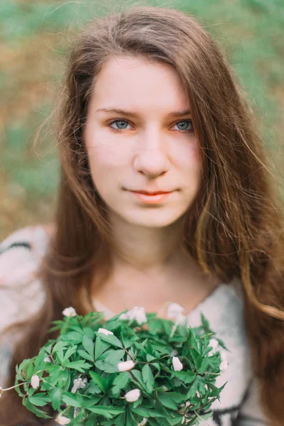 Bella ragazza che tiene fiori bianchi primaverili a piedi attraverso la foresta verde — Foto Stock