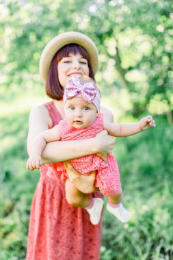 Hasır şapkalı güzel anne ve küçük kızı açık havada pembe bir elbise içinde. Mutlu bir ailenin açık hava portresi. Aile görünüşü. Mutlu anne kızıyla eğleniyor.