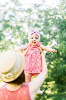 Hasır şapkalı güzel anne ve küçük kızı açık havada pembe bir elbise içinde. Genç anne güneşli bir günde bebeği gökyüzüne kusar..