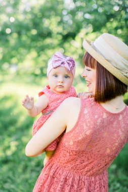 Hasır şapkalı güzel anne ve küçük kızı açık havada pembe bir elbise içinde. Mutlu bir ailenin açık hava portresi. Aile görünüşü. Anne ve kızı yaz parkında..