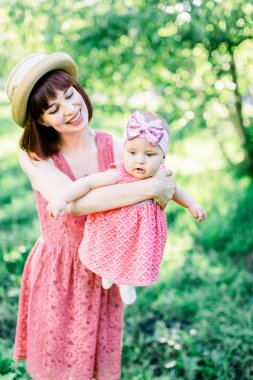 Hasır şapkalı güzel anne ve küçük kızı açık havada pembe bir elbise içinde. Mutlu bir ailenin açık hava portresi. Aile görünüşü. Anne ve bebek park portresinde