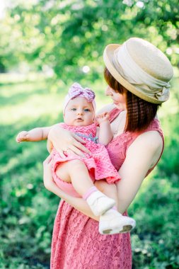 Hasır şapkalı güzel anne ve küçük kızı açık havada pembe bir elbise içinde. Mutlu bir ailenin açık hava portresi. Aile görünüşü. Anne ve bebek park portresinde