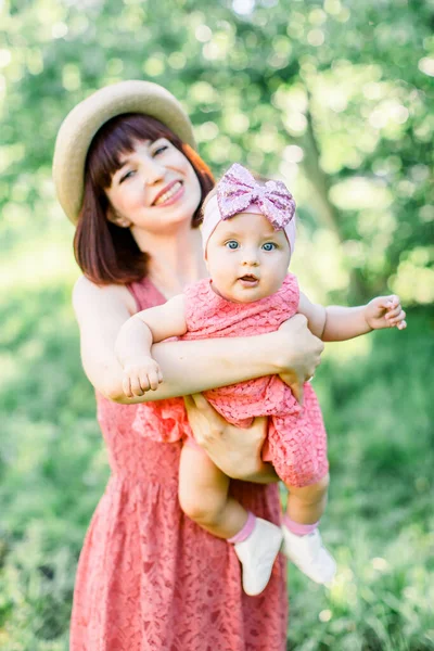 Beautiful Mother with the straw hat And her little daughter outdoors family look in in a pink dress . Outdoor Portrait of happy family. family look. Happy mother having fun with her daughter — Stock Photo, Image