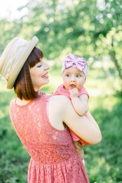 Красива мати з солом'яним капелюхом І її маленька донька на відкритому повітрі сімейство дивляться в рожеве плаття. На відкритому повітрі Портрет щасливої родини. сімейний погляд. Мати і її дочка в літньому парку . — стокове фото