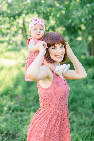 Beautiful Mother with the straw hat And her little daughter outdoors family look in in a pink dress . family look. small child, a little girl sits on the shoulders of mom smiling — Stock Photo, Image