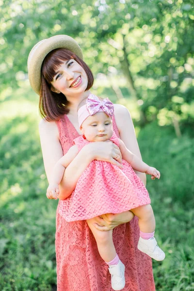 藁帽子の美しい母と彼女の小さな娘屋外の家族はピンクのドレスで見ています。若いです母とともに彼女の小さな赤ちゃんでザ牧草地 — ストック写真