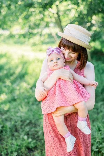 藁帽子の美しい母と彼女の小さな娘屋外の家族はピンクのドレスで見ています。若いです母とともに彼女の小さな赤ちゃんでザ牧草地 — ストック写真