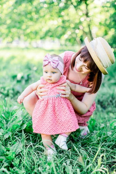 緑の草、サポート歩くことを学ぶことで彼女の手を繋いで母親に彼の最初のステップを作るかわいい面白い幸せな赤ちゃん — ストック写真