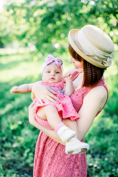 藁帽子の美しい母と彼女の小さな娘屋外の家族はピンクのドレスで見ています。幸せな家族の屋外肖像画。家族みたいに公園の肖像画の母親と赤ちゃん — ストック写真