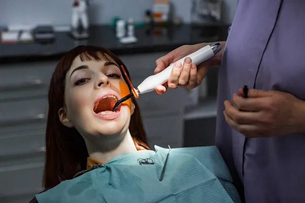 Jonge vrouw patiënt die tandheelkundige behandeling bij tandartsen kantoor. Tandarts assistent met behulp van tandheelkundige behandeling met tandheelkundige uitharding Uv lamp op de tanden van de patiënten — Stockfoto
