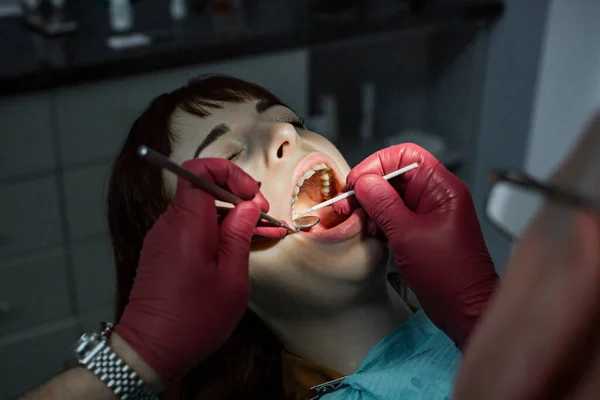 Exame dentário extenso. Foto de perto de uma jovem mulher com os dentes examinados por um dentista profissional usando luvas médicas vermelhas. Conceito odontológico oral — Fotografia de Stock