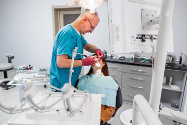 Uzman kıdemli dişçinin genç bayan hastası için dişçi muayenehanesinde tedavi uygulamasının yan görüntüsü..