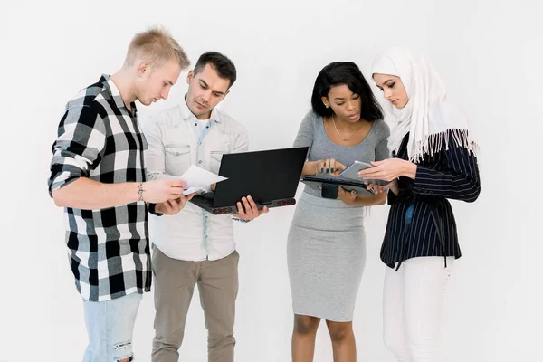 Група з чотирьох етнічних студентів, які працюють над навчанням разом, використовуючи ноутбук і планшет, стоять на білому тлі. Міжнародний бізнес, концепція освіти — стокове фото
