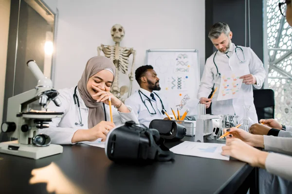 Çok ırklı tıp öğrencileri olan yakışıklı bir erkek profesör ya da sınıfta laboratuvar önlüğü giyen bilim adamları. Genç güzel Müslüman kız mutlu ve gülümsüyor. — Stok fotoğraf