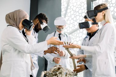 Çok ırklı tıp öğrencileri ya da doktorlar ve yetişkin erkek profesörlerden oluşan bir grup, insan iskeleti anatomisi üzerine çalışan, VR gözlükleri kullanan bir grup. Tıp, anatomi, vr konsepti