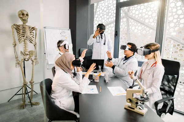 Группа мультиэтнических творческих врачей-исследователей носит очки VR, жестикулирует, симулируя работу над виртуальным интерфейсом в современной лаборатории. Наука, медицина, концепция vr — стоковое фото
