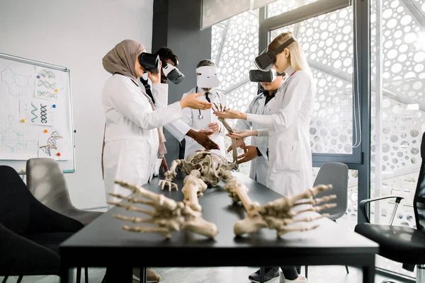 Professor do sexo masculino usando óculos de realidade virtual para ensinar anatomia esquelética para estudantes multiétnicos em sala de aula. Educação, RV, Tutoria, Novas Tecnologias e Métodos de Ensino conceito . — Fotografia de Stock