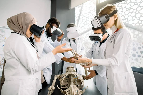 Grupo de jovens estudantes de medicina multiétnica ou médicos vestindo óculos VR estudando anatomia do esqueleto humano em sala de aula moderna. Medicina, anatomia, conceito de realidade virtual — Fotografia de Stock