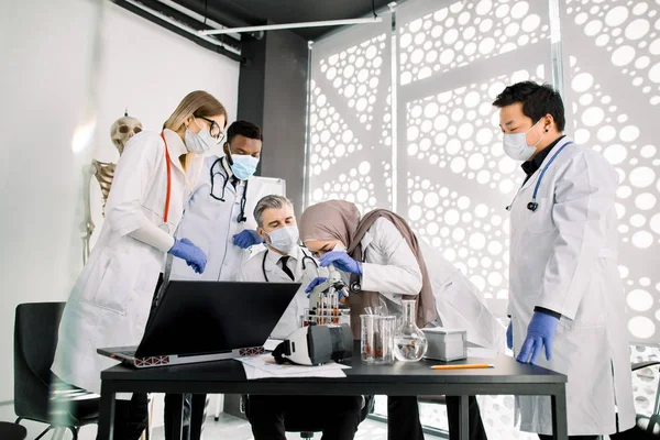 Equipe de cientistas médicos bioquímicos que trabalham com microscópio, fazendo experimentos científicos de pesquisa em laboratório. Mulher muçulmana está olhando através do microscópio e discutindo com colegas — Fotografia de Stock