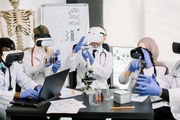 Cientistas médicos de casacos. luvas e usando óculos de realidade virtual trabalhando em laboratório, fazendo pesquisas médicas. Biotecnologia, química, ciência, experimentos e conceito de saúde — Fotografia de Stock