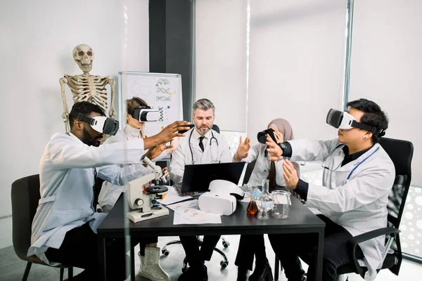 Biyoteknoloji, kimya, bilim, sağlık, VR konsepti. Tıbbi teşhis uzmanları, bilim adamları, VR gözlük takan doktorlar yeni maddeleri analiz ediyor, modern laboratuarda yeni bir proje üzerinde çalışıyorlar. — Stok fotoğraf
