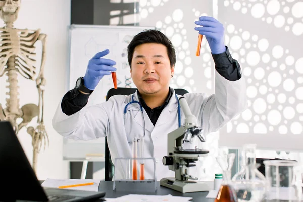 Sorrindo cientista homem asiático ou médico testando novas drogas para prevenir e destruir novas estirpes do vírus ou bactérias, detém dois tubos de vidro. Conceito de pesquisa e medicina farmacêutica . — Fotografia de Stock