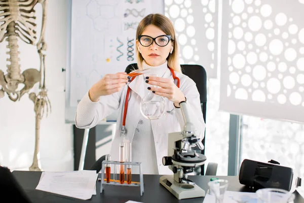 Pretty Caucasian woman researcher doctor chemist with glass equipment in the lab. Female professional scientist purifying red solution form tube into glass flask. Laboratory, clinical analysis concept — стокове фото