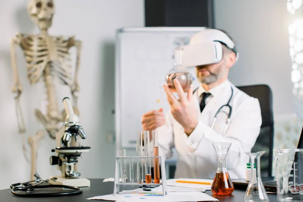 VR gözlük takan ve elinde matarayla klinik laboratuarında test yapan bilim adamını yakından çek. Sanal gerçeklik gözlüğü takan doktor bilim adamı yeni aşı ya da uyuşturucu araştırması yapıyor. — Stok fotoğraf