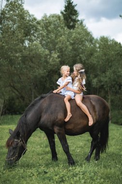 Çocuklar dağlarda ata biniyor. At çiftliğinde aile tatili. Çocuklar ata biner. Çocuk ve evcil hayvan. Küçük kızlar atlarıyla dışarıda dolaşırken eğleniyorlar.