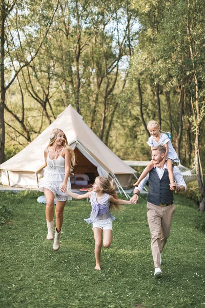 Šťastná bělošská rodina, otec matka a dvě malé dcery, baví venku v parku nebo kempování, užívají si čas a společně se smějí, drží se za ruce a běhají. Koncept lásky a rodičovství — Stock fotografie