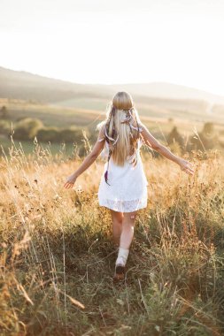 Uzun sarı saçlı, beyaz elbiseli ve kovboy çizmeli yaz hippisi kız. Arka plan