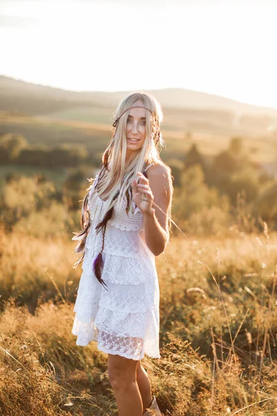 Bela jovem boho menina em vestido branco em pé ao ar livre durante o pôr do sol de verão no campo ou montanhas . — Fotografia de Stock