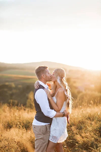 Homem bonito e mulher bonita em roupas elegantes boho rústico, beijando. Casal encantador no estilo rústico eco boho, de pé no campo de verão. Beijando momento sensual — Fotografia de Stock