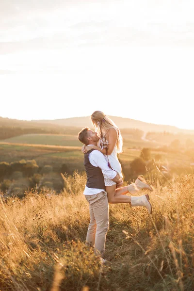 Снимок молодой хиппи-девушки, которую носит её красавчик-бойфренд на летнем поле. Пара веселится в летний вечер на свежем воздухе — стоковое фото
