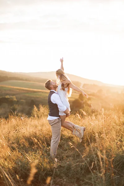 Shot of young boho hippie woman being carried by her handsome boyfriend in summer field. Couple having fun on their summer evening outdoors Stock Picture