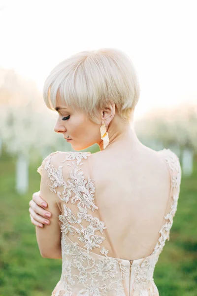 Vue de dos portrait de jolie jeune femme blonde en robe élégante, marchant dans le jardin de printemps parmi les arbres à fleurs — Photo