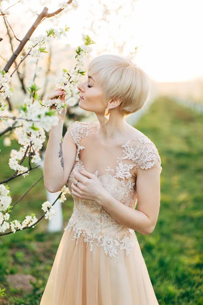 Belle jeune femme heureuse en robe de mariée élégante de luxe profitant de l'odeur dans un jardin printanier fleuri. Jardin fleuri de printemps sur le fond — Photo