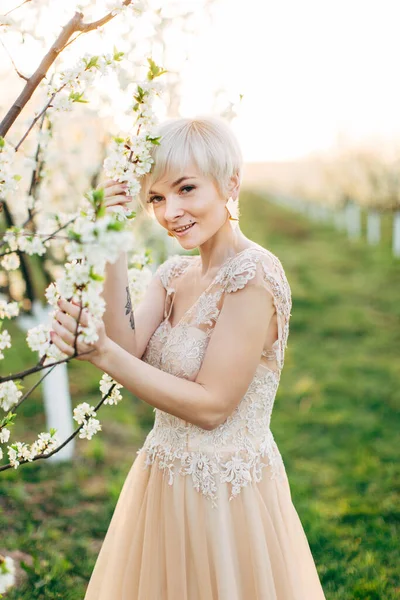 Portrait de jeune femme blanche blonde en robe élégante posant dans le jardin fleuri au printemps. Jeune belle mariée dans le jardin fleuri . — Photo