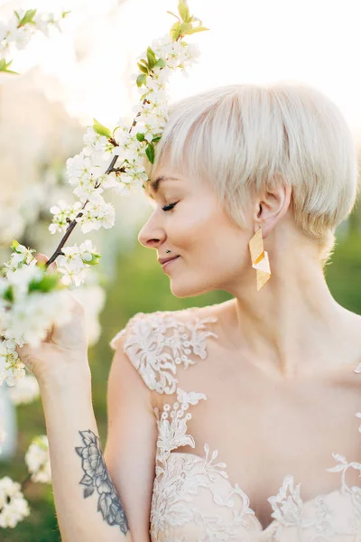 Portrait de profil rapproché de belle femme blonde dans une élégante robe de luxe marchant au printemps du jardin fleuri, touchant la branche de l'arbre et fermant les yeux — Photo