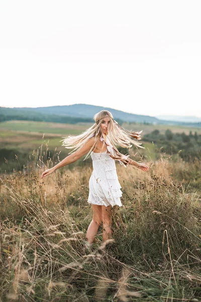 Mulher modelo de moda retrato ao ar livre no campo de verão, pôr do sol. Boho estilo jovem mulher em vestido branco e com cobertura para a cabeça feita de penas — Fotografia de Stock