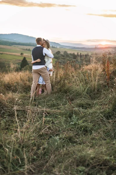 Joyeux jeune famille avec deux enfants à l'extérieur dans le champ de coucher de soleil d'été. Jeune couple de parents embrassant dans un champ, petites filles mignonnes les embrassant. Famille, amour, moments heureux — Photo