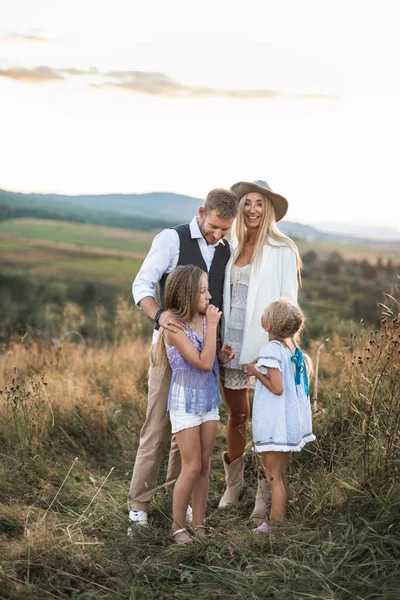 Mutlu gülümseyen genç aile, baba, anne ve iki küçük kız dışarıda eğleniyor, vahşi bir tarlada birlikte duruyorlar. Anne ve baba çocuklarıyla konuşuyor, gülüyor, birlikte eğleniyorlar. — Stok fotoğraf