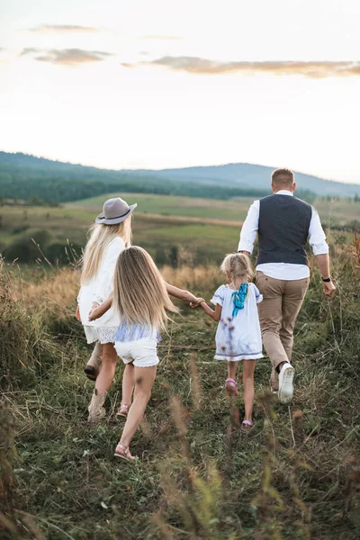 Mãe e pai brincando com seus filhos filhas no campo, correndo e rindo, vista traseira. Conceito de estilo de vida familiar feliz . — Fotografia de Stock